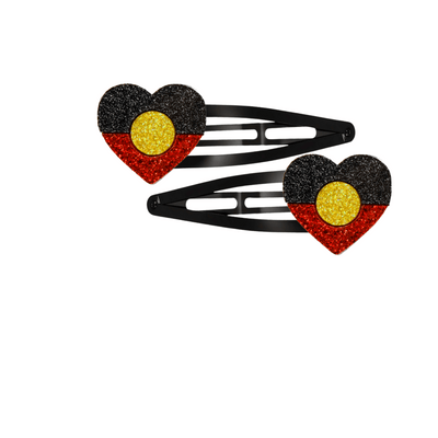 An Image of Haus of Dizzy's Heart Shaped Glitter Aboriginal Flag Hair Clips. Flags are on Black Hair Clips