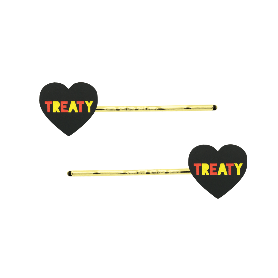 An Image of Haus of Dizzy's Black Acrylic Heart Shaped Hair Pins with "Treaty" text in Red and Yellow. Hearts are on Gold Pins
