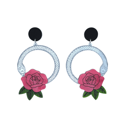 An image of Haus of Dizzy's large Snake Rose hoop dangle earrings, featuring a silver snake in a circle with a flamingo pink rose and matte black circle top.