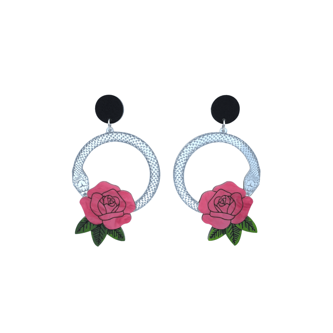 An image of Haus of Dizzy's small Snake Rose hoop dangle earrings, featuring a silver snake in a circle with a light flamingo rose and matte black circle top.