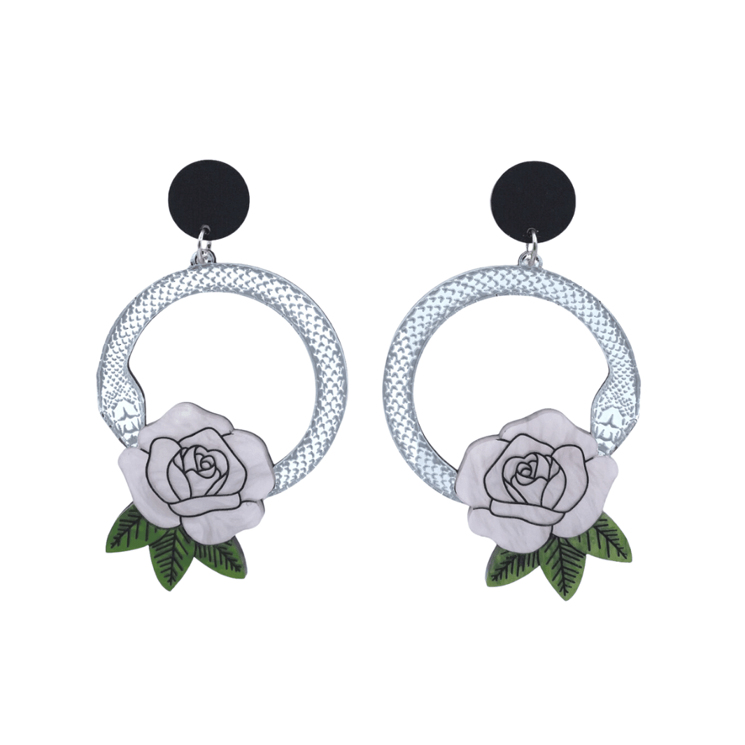 An image of Haus of Dizzy's large Snake Rose hoop dangle earrings, featuring a silver snake in a circle with a light pink rose and matte black circle top.