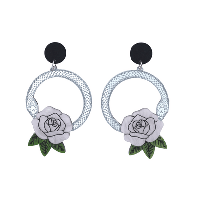 An image of Haus of Dizzy's large Snake Rose hoop dangle earrings, featuring a silver snake in a circle with a light pink rose and matte black circle top.