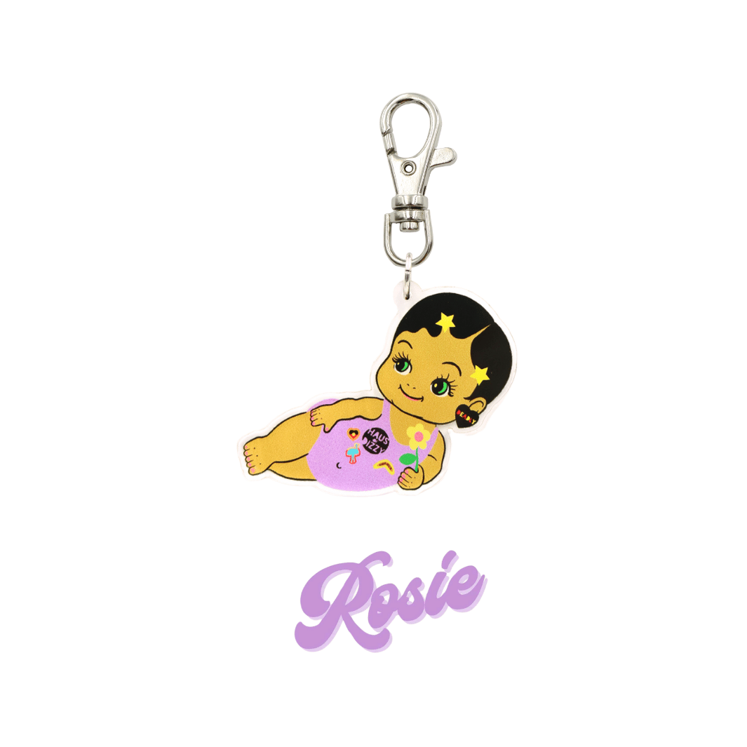 An image of Haus of Dizzy's Dizzy Chicks acrylic keyring, with a doll with short black pixie hair and gold star hair clips in a purple one piece playsuit and Deadly acrylic heart earrings on a parrot clasp. Purple Colour "Rosie" Cursive Text is at the bottom of the image. 