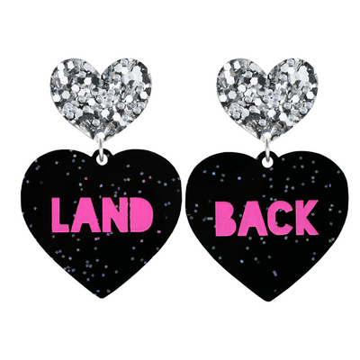 An image of Haus of Dizzy's large Land Back heart shaped dangle earrings, with Hot Pink Land Back text on Black Chunky Glitter acrylic and a Silver Glitter heart top.
