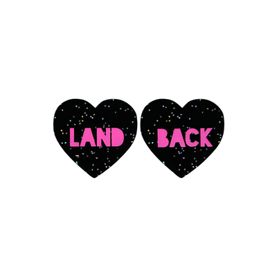 An image of Haus of Dizzy's Small ‘Land Back’ heart shaped dangle earrings, with Hot Pink “Land Back” text on a Black Glitter acrylic stud heart.