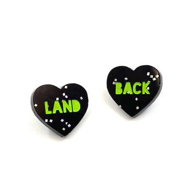 Image of Haus of Dizzy's acrylic black glitter etched studs with green 'LAND BACK' paint fill text. 