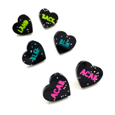 Image of Haus of Dizzy's acrylic black glitter etched studs with blue 'BLM', pink 'ACAB', green 'LAND BACK' paint fill text. 