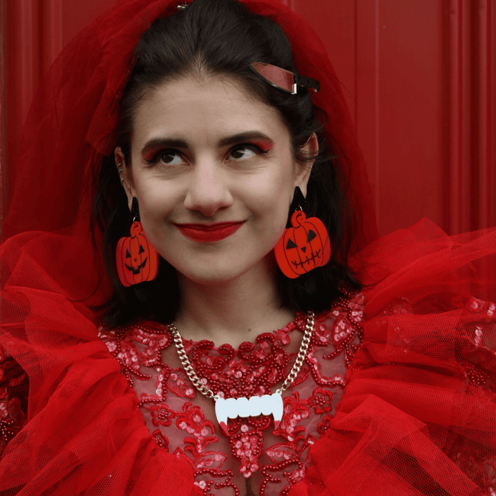 model in a red halloween bride costume wearing haus of dizzy spooky squash pumpkin earrings against a red background