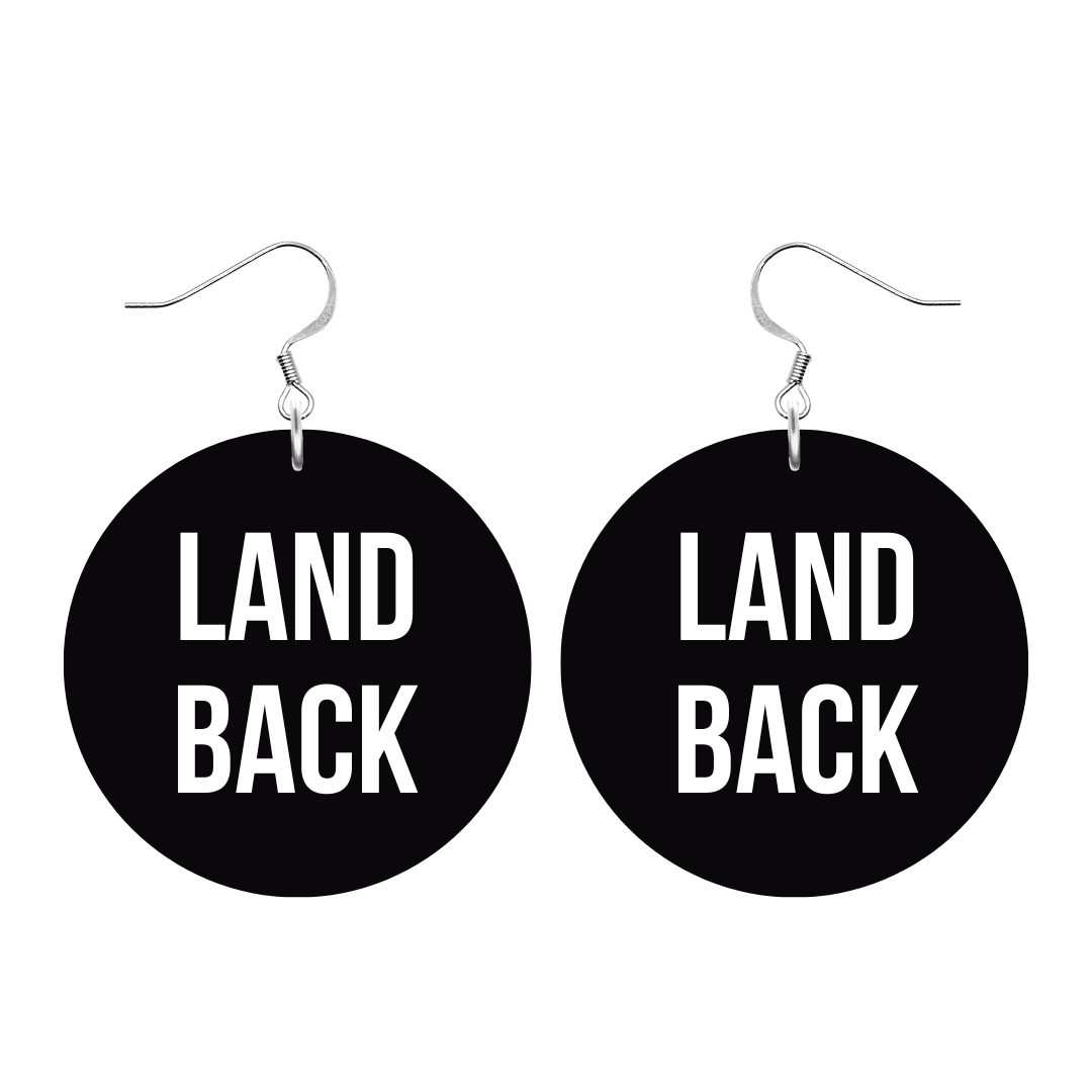 An image of Haus of Dizzy's ‘Land Back’ circle shaped dangle earrings, with white paint fill Land Back text on black acrylic and a silver hook top.