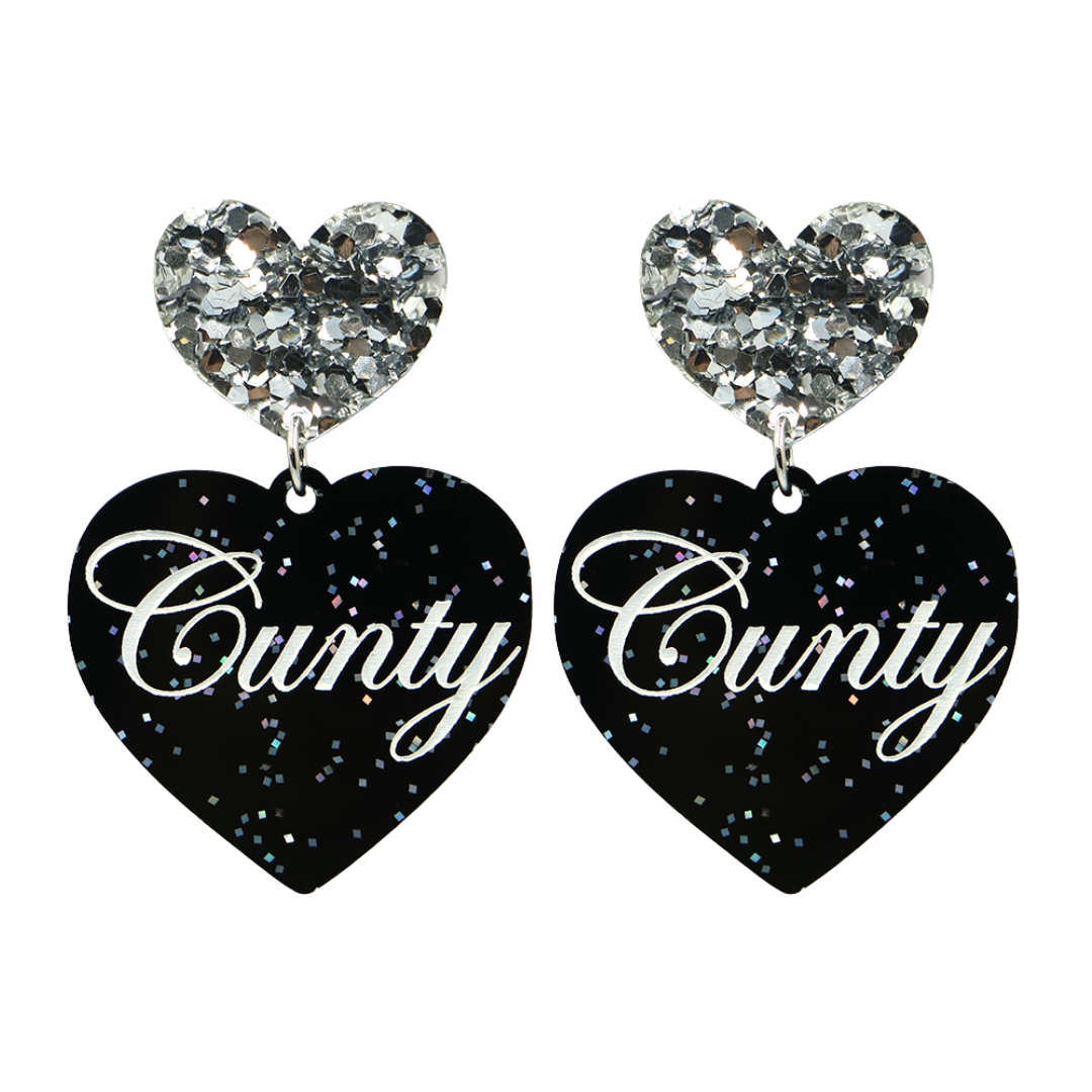 Black glitter Heart-shaped earrings with white text that says 'Cunty', and silver glitter heart tops on a white background