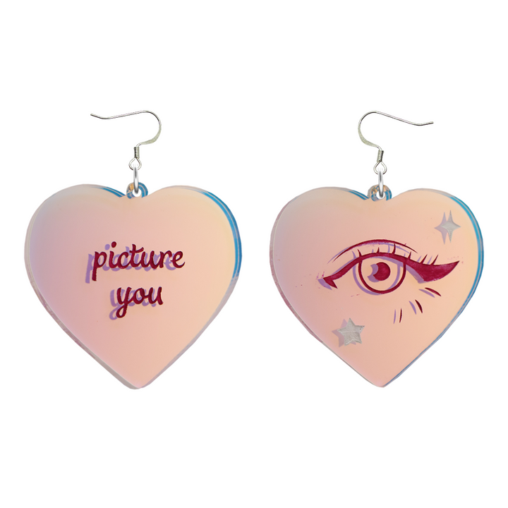 haus of dizzy heart-shaped iridescent earrings with 'picture you' text on one and eye design on the other. on silver hooks. they are on a white background. size large