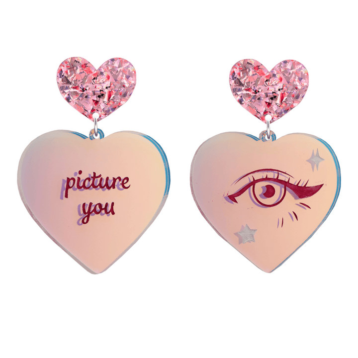haus of dizzy heart-shaped iridescent earrings with 'picture you' text on one and eye design on the other. pink red chunky glitter heart tops. they are on a white background. size large