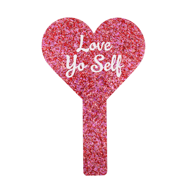Pink glittery heart-shaped mirror with 'Love Yo Self' text on a white background. image of the back of the mirror.