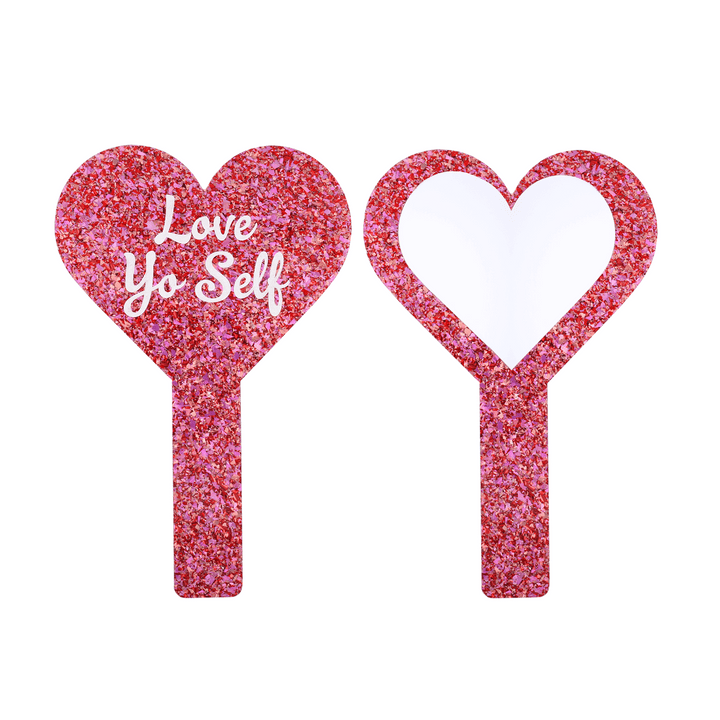 Front and back image of pink glittery heart-shaped mirror with 'Love Yo Self' text one one side, and mirror piece on the other. They are on a white background
