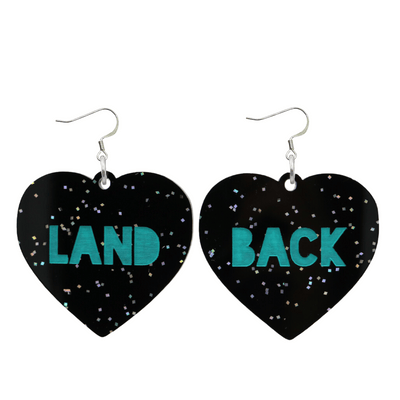 An image of Haus of Dizzy's large Land Back heart shaped dangle earrings, with Emerald Green Land Back text on Black Chunky Glitter acrylic and a hook top.