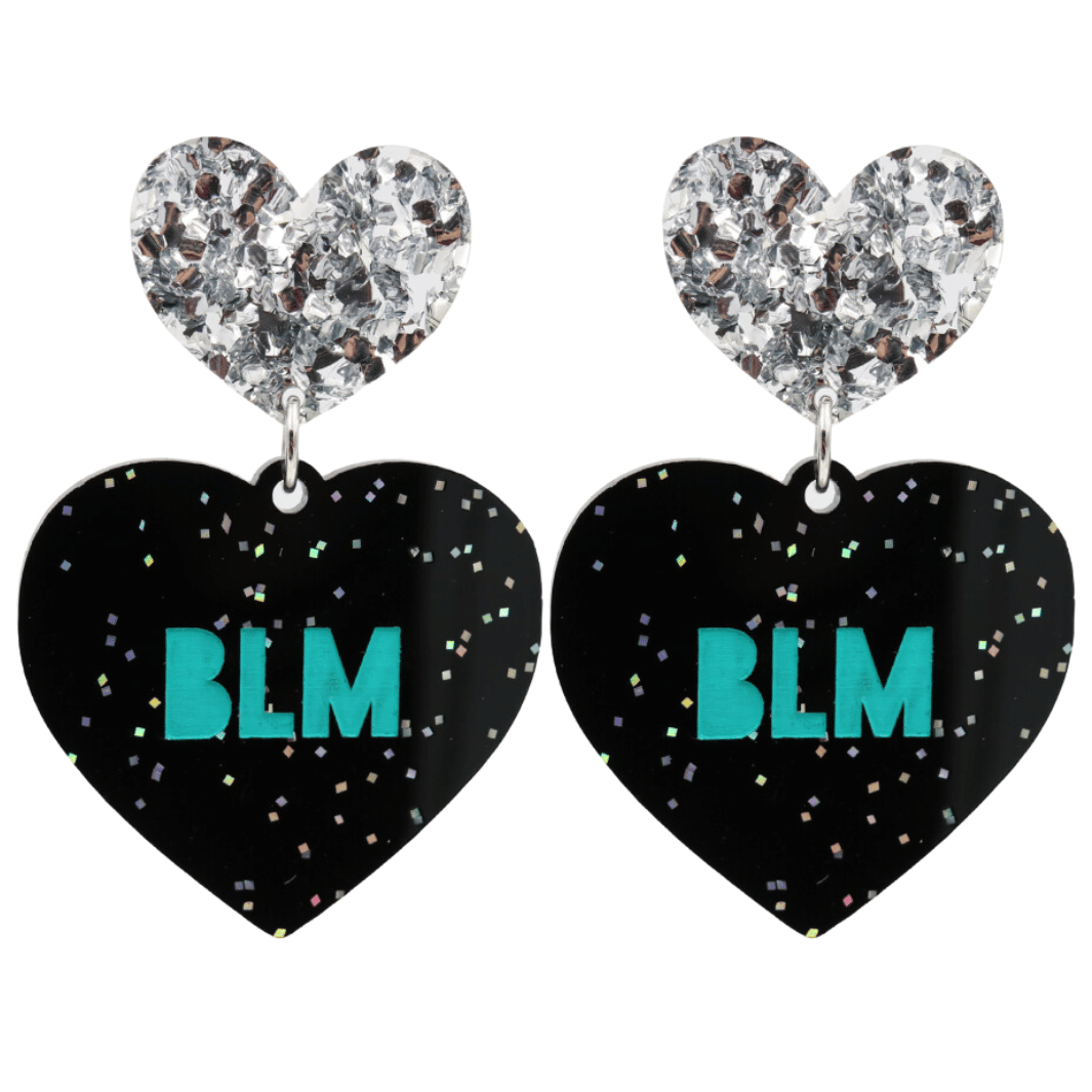 An image of Haus of Dizzy's Large ‘BLM’ heart shaped dangle earrings, with Emerald Green  “BLM’ text on Black Glitter acrylic and a Silver Glitter heart top.