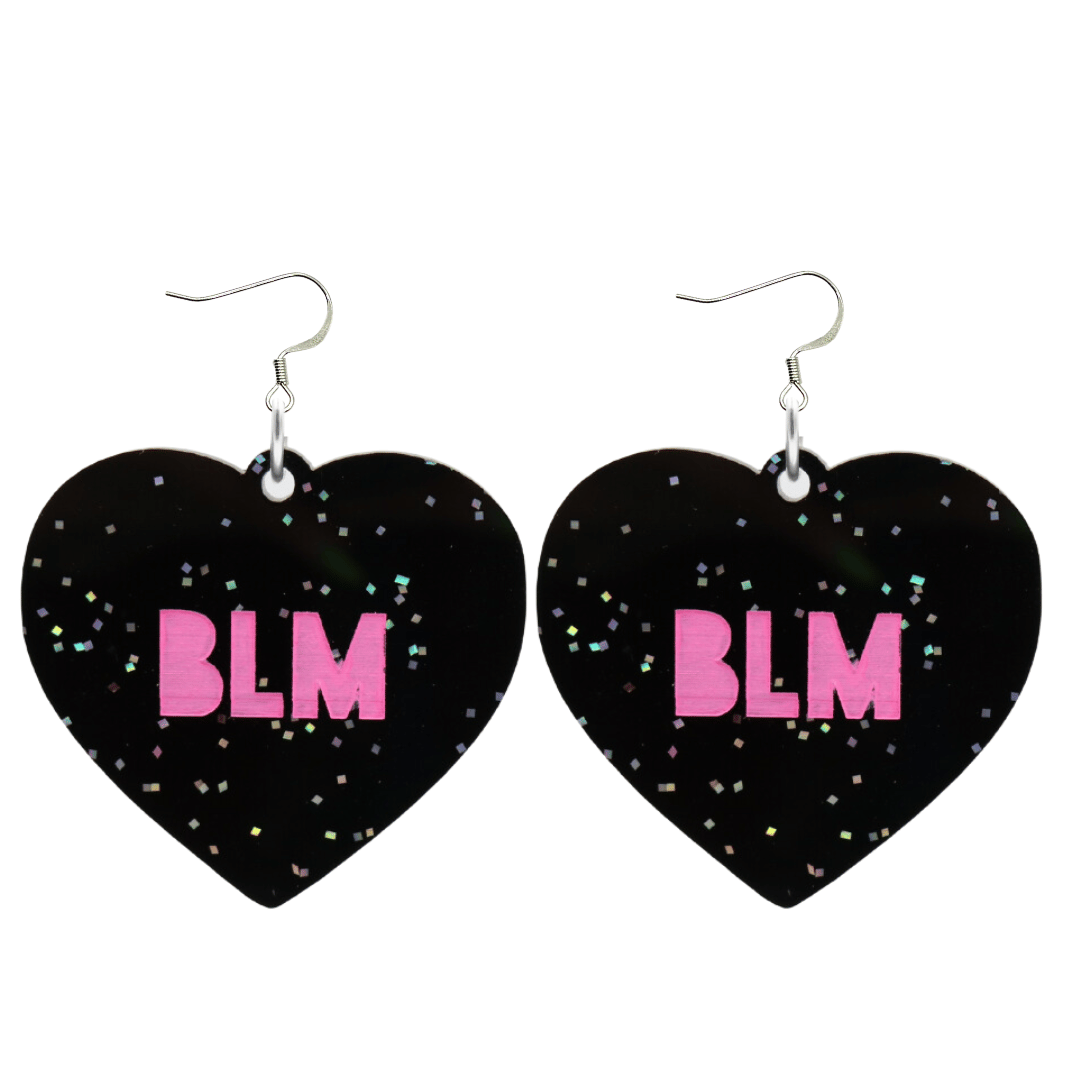 An image of Haus of Dizzy's Large ‘BLM’ heart shaped dangle earrings, with Hot Pink  “BLM’ text on Black Glitter acrylic on Hooks
