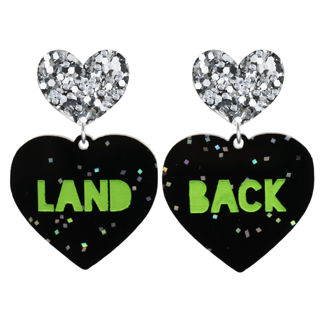 An image of Haus of Dizzy's large Land Back heart shaped dangle earrings, with Apple Green Land Back text on Black Chunky Glitter acrylic and a Silver Glitter heart top.