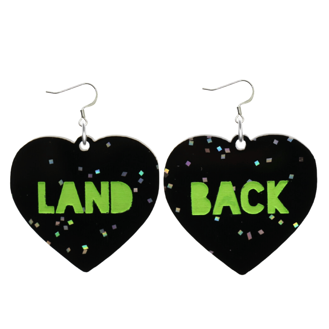 An image of Haus of Dizzy's large Land Back heart shaped dangle earrings, with Apple Green Land Back text on Black Chunky Glitter acrylic and a hook top.