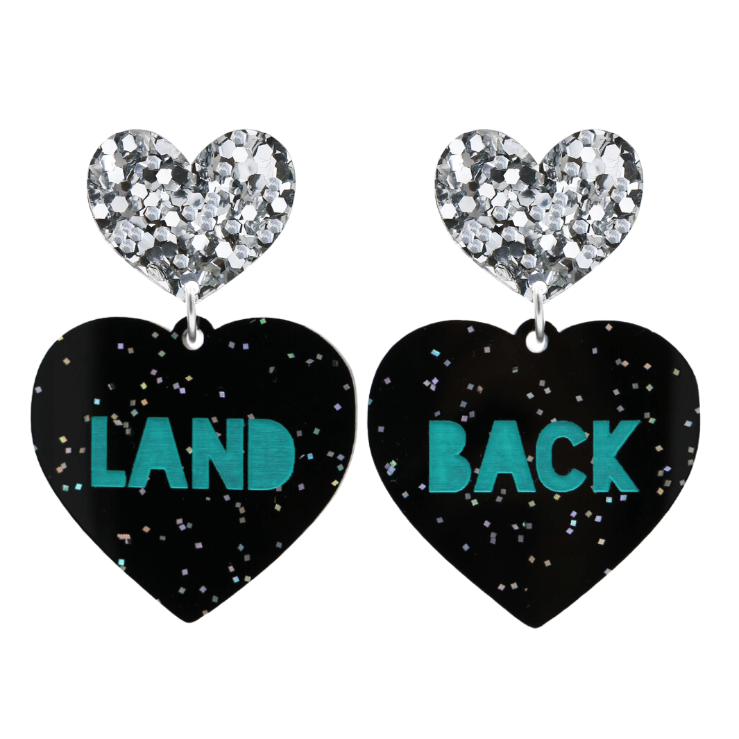 An image of Haus of Dizzy's large Land Back heart shaped dangle earrings, with Emerald Green Land Back text on Black Chunky Glitter acrylic and a Silver Glitter heart top.