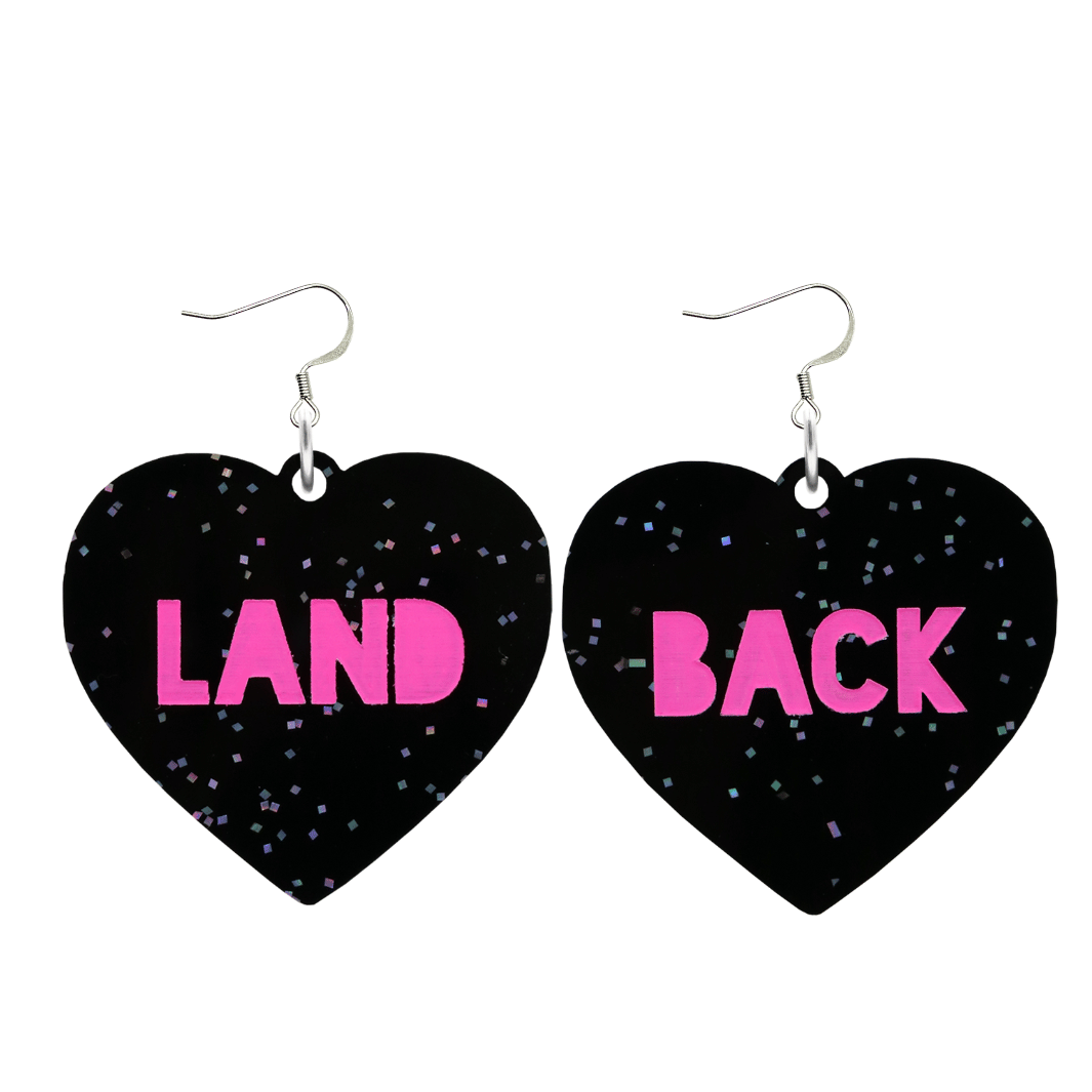 An image of Haus of Dizzy's large Land Back heart shaped dangle earrings, with Hot Pink Land Back text on Black Chunky Glitter acrylic and a hook top.