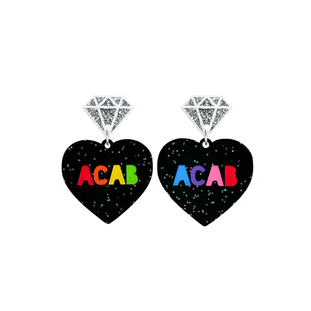 An image of Haus of Dizzy's small 'F U ACAB' heart-shaped dangle earrings, with “ACAB” rainbow text on black glitter acrylic and a silver mirror diamonds top.