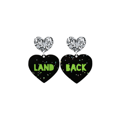 An image of Haus of Dizzy's small Land Back heart shaped dangle earrings, with Apple Green Land Back text on Black Chunky Glitter acrylic and a Silver Glitter heart top.