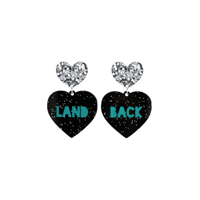 An image of Haus of Dizzy's small Land Back heart shaped dangle earrings, with Emerald Green Land Back text on Black Chunky Glitter acrylic and a Silver Glitter heart top