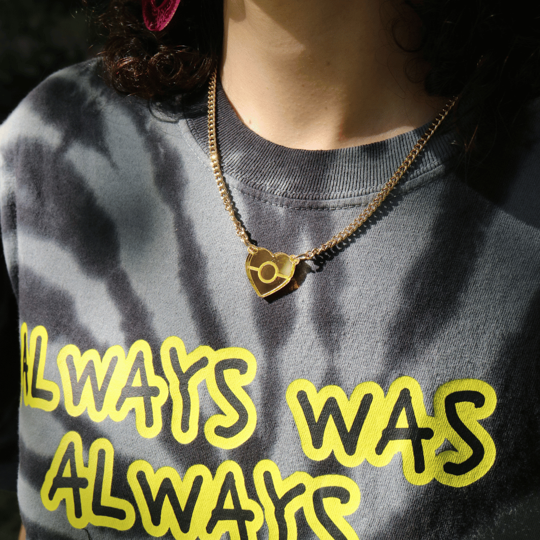 close up image of haus of dizzy mini mirror aboriginal flag pendant necklace on a model, wearing a grey tie dye t shirt. the necklace is reflecting in the sun