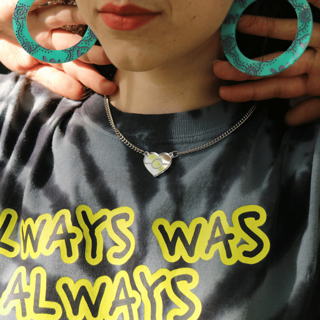 model wearing haus of dizzy wiradjuri yinaa turquoise hoop earrings and aboriginal flag mini mirror pendant necklace. they are wearing a grey tie dye shirt with text 'ALWAYS WAS ALWAYS WILL BE'