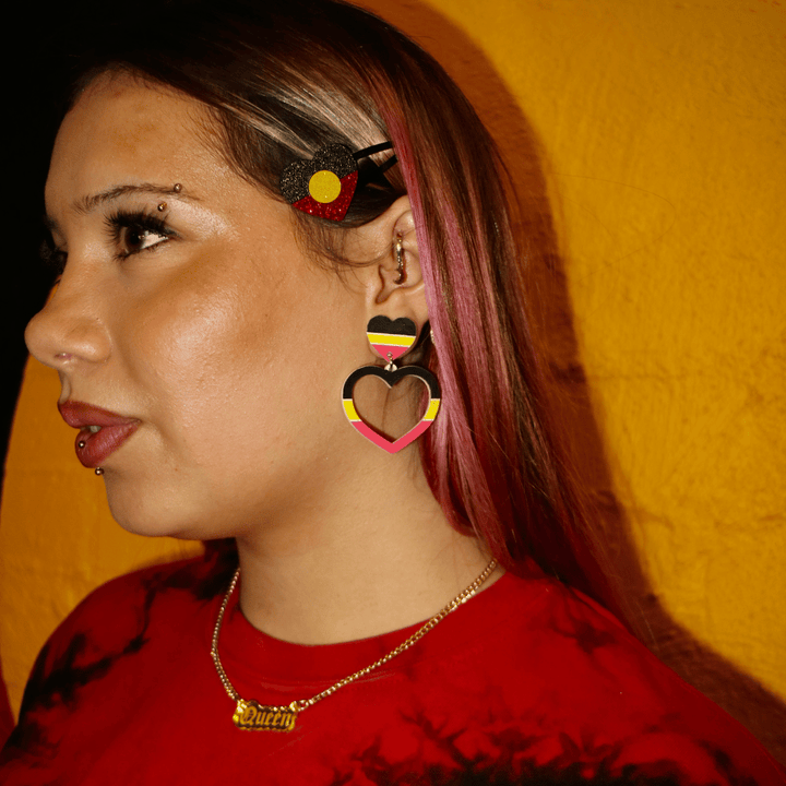 model wearing haus of dizzys hand painted aboriginal flag coloured barbie heart earrings looking away from camera