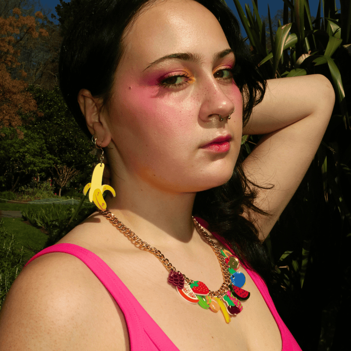 side profile shot of model wearing haus of dizzys split banana earrings and fruit salad charm necklace.