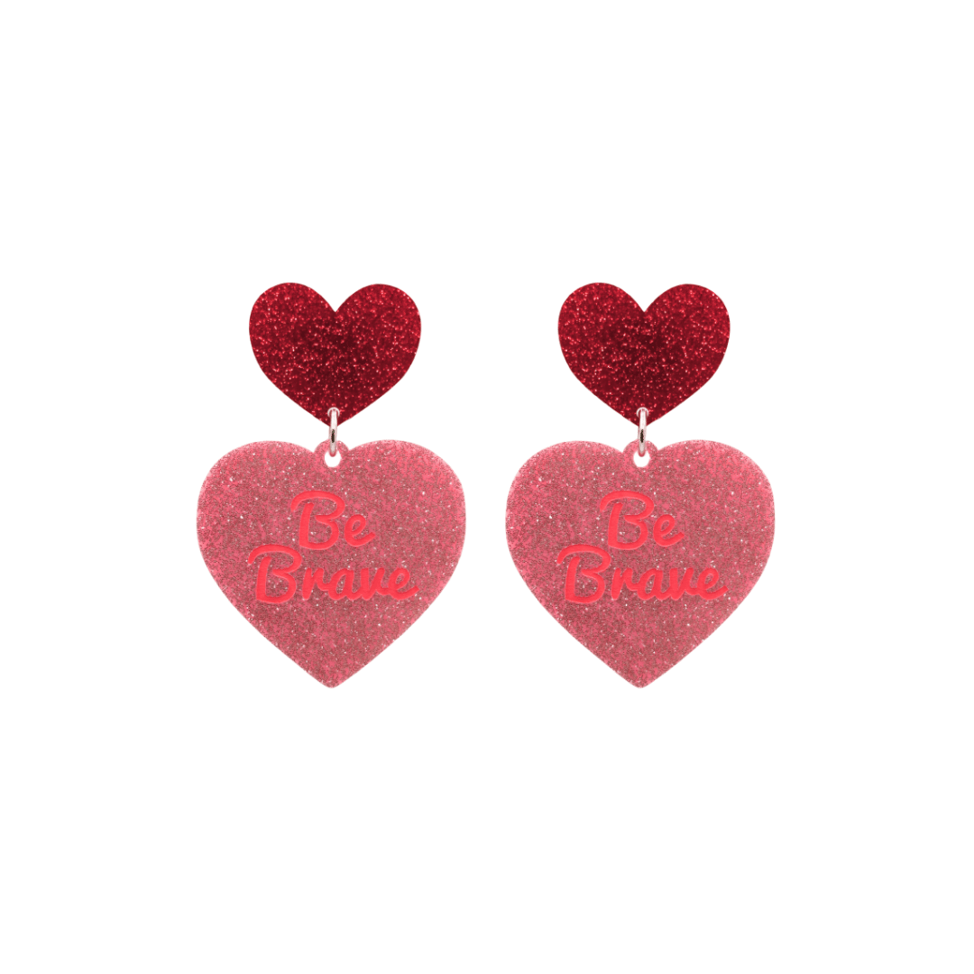 haus of dizzy baby pink glitter heart-shaped acrylic earrings with bright red 'Be Brave' text and red glitter heart tops size small