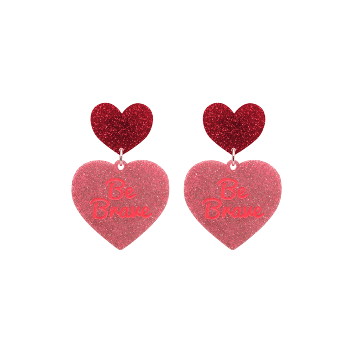 haus of dizzy baby pink glitter heart-shaped acrylic earrings with bright red 'Be Brave' text and red glitter heart tops size small