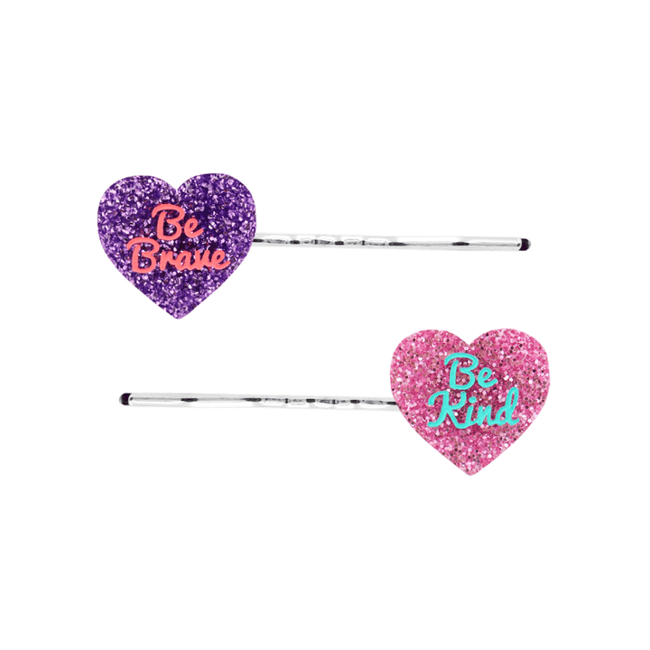 haus of dizzy heart shaped acrylic hair pins, one purple glitter with red 'be brave' text, the other pink glitter with aqua 'be kind' text, both on silver bobby hair pins
