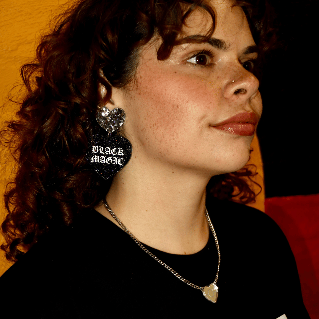 close up of Aboriginal model wearing haus of dizzy black magic heart earrings with BLACK MAGIC written in white paint with old english font