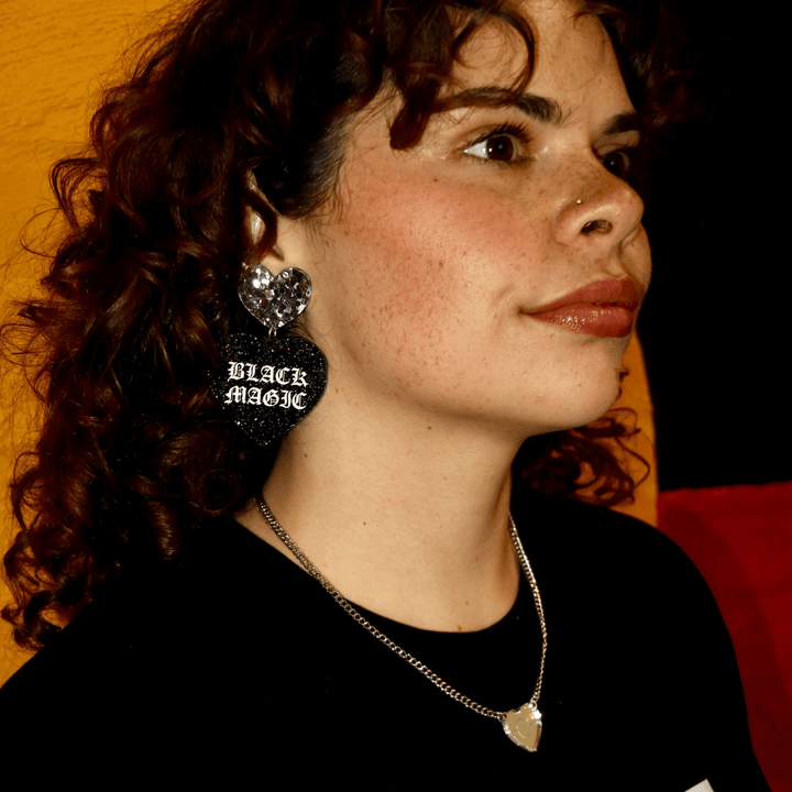 close up of Aboriginal model wearing haus of dizzy black magic heart earrings with BLACK MAGIC written in white paint with old english font