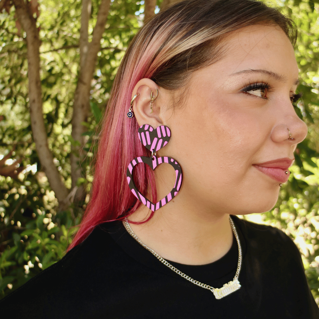 model wearing haus of dizzy blak collection heart hoop earrings in markings. close up image of model's side profile with the black earrings with hot pink hand painted detailing of aboriginal symbols.