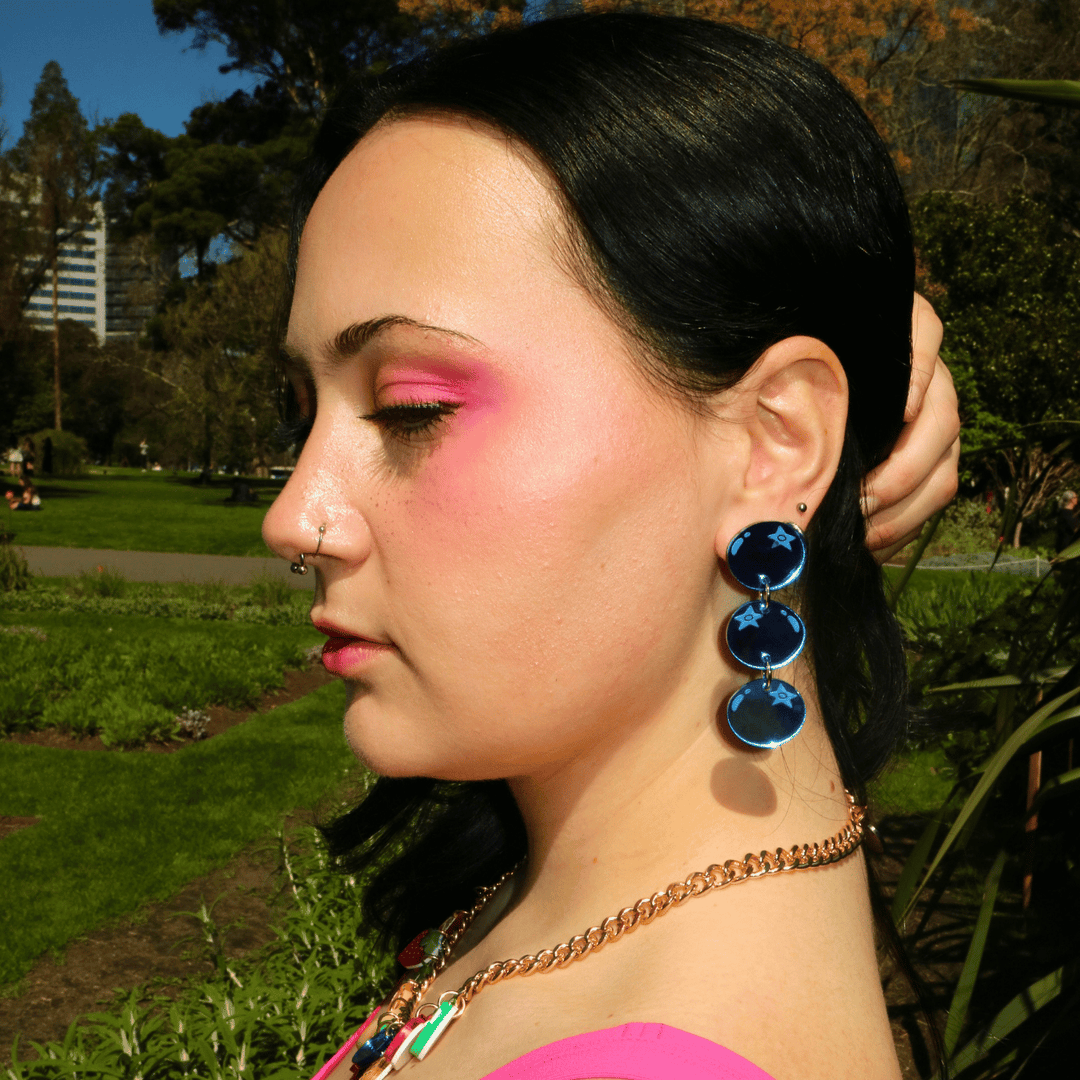 side profile shot of model wearing haus of dizzy's berry blue stacked blueberry earrings while holding hair out of face. the blueberries are made out of blue mirror acrylic.