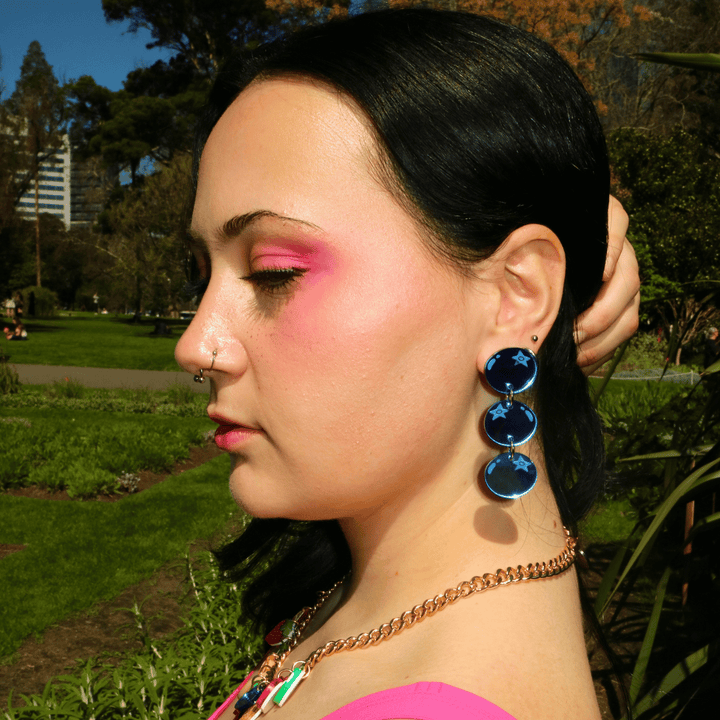 side profile shot of model wearing haus of dizzy's berry blue stacked blueberry earrings while holding hair out of face. the blueberries are made out of blue mirror acrylic.