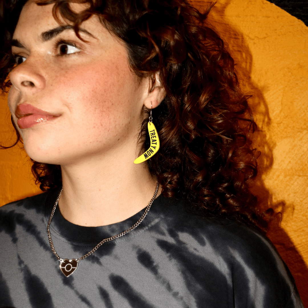 model wearing haus of dizzy yellow boomerang earrings that read 'treaty now' in bold black text