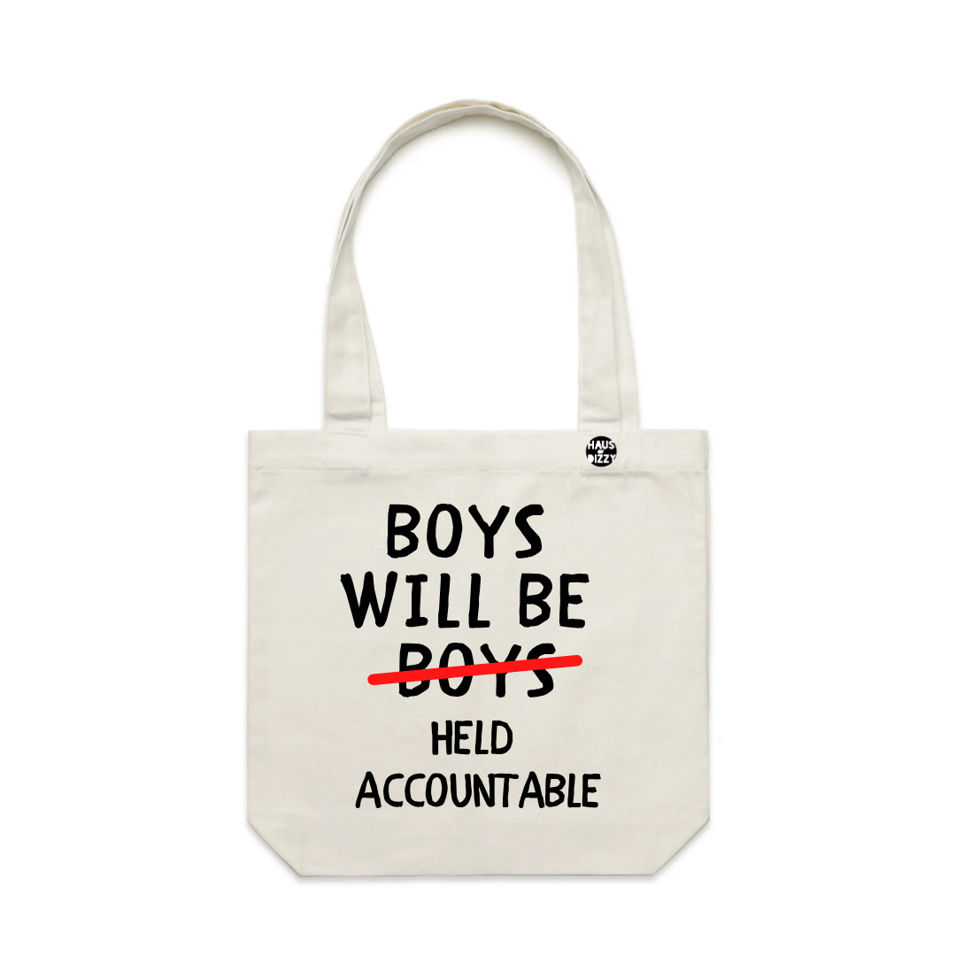 haus of dizzys off-white canvas tote bag with black text reading 'BOYS WILL BE BOYS' and a red line crossing out 'BOYS', followed by 'HELD ACCOUNTABLE' in black. A small circular logo is printed near the top right handle on a plain white background.