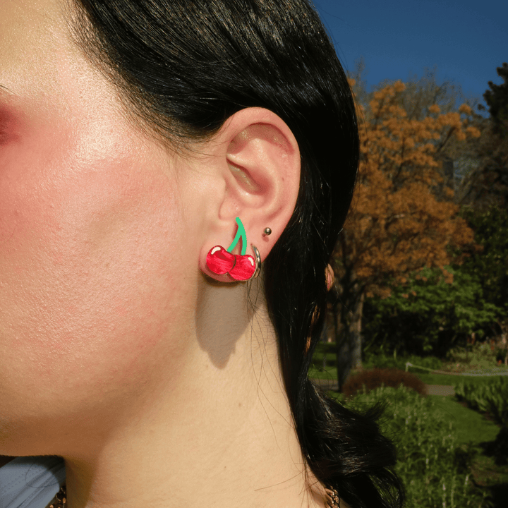 close up side shot of model wearing haus of dizzy cherry studs using red ripple acrylic and matte green acrylic.