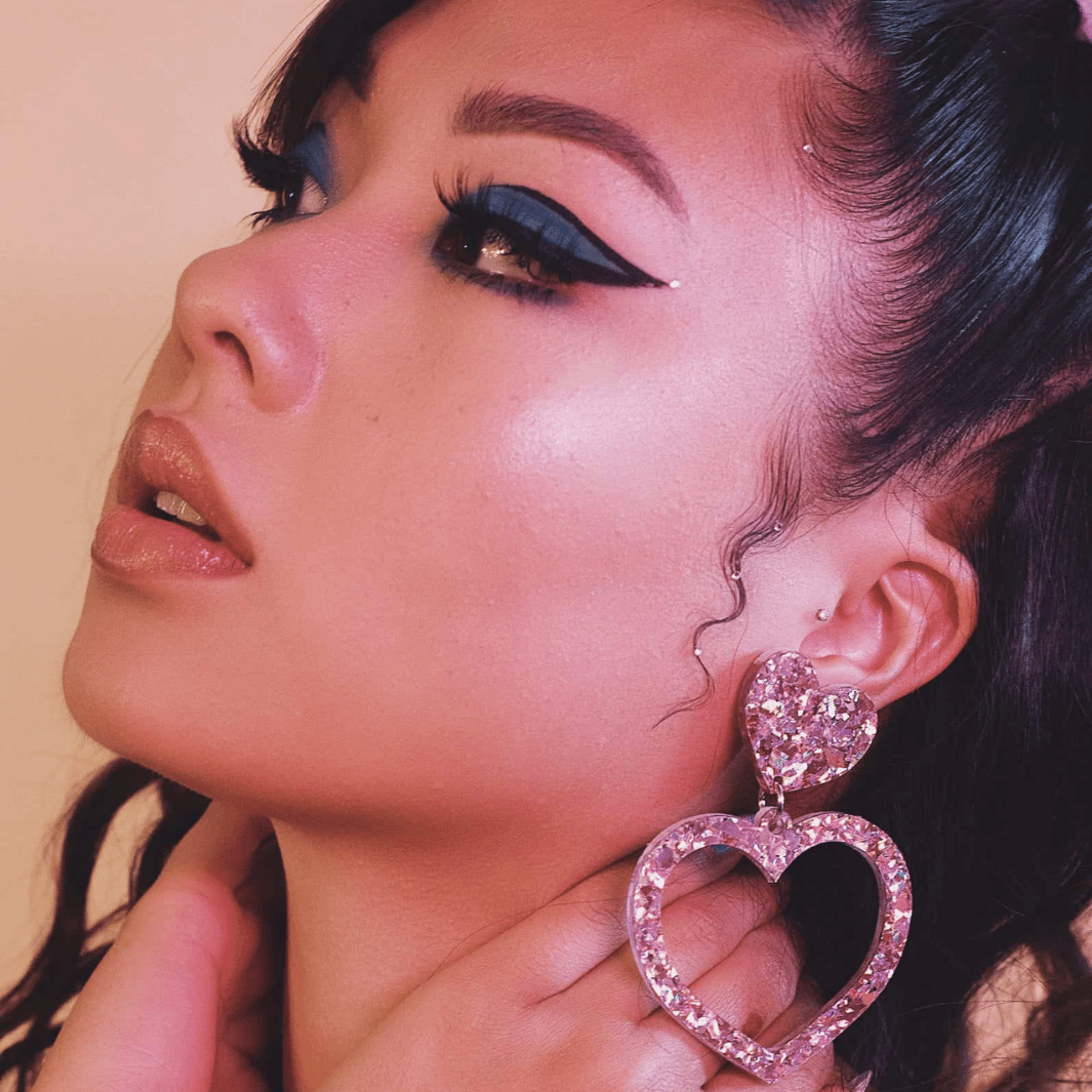 close up of model looking away to side wearing haus of dizzy crystal barbie hearts in rose quartz with 60s mod blue graphic eyeliner