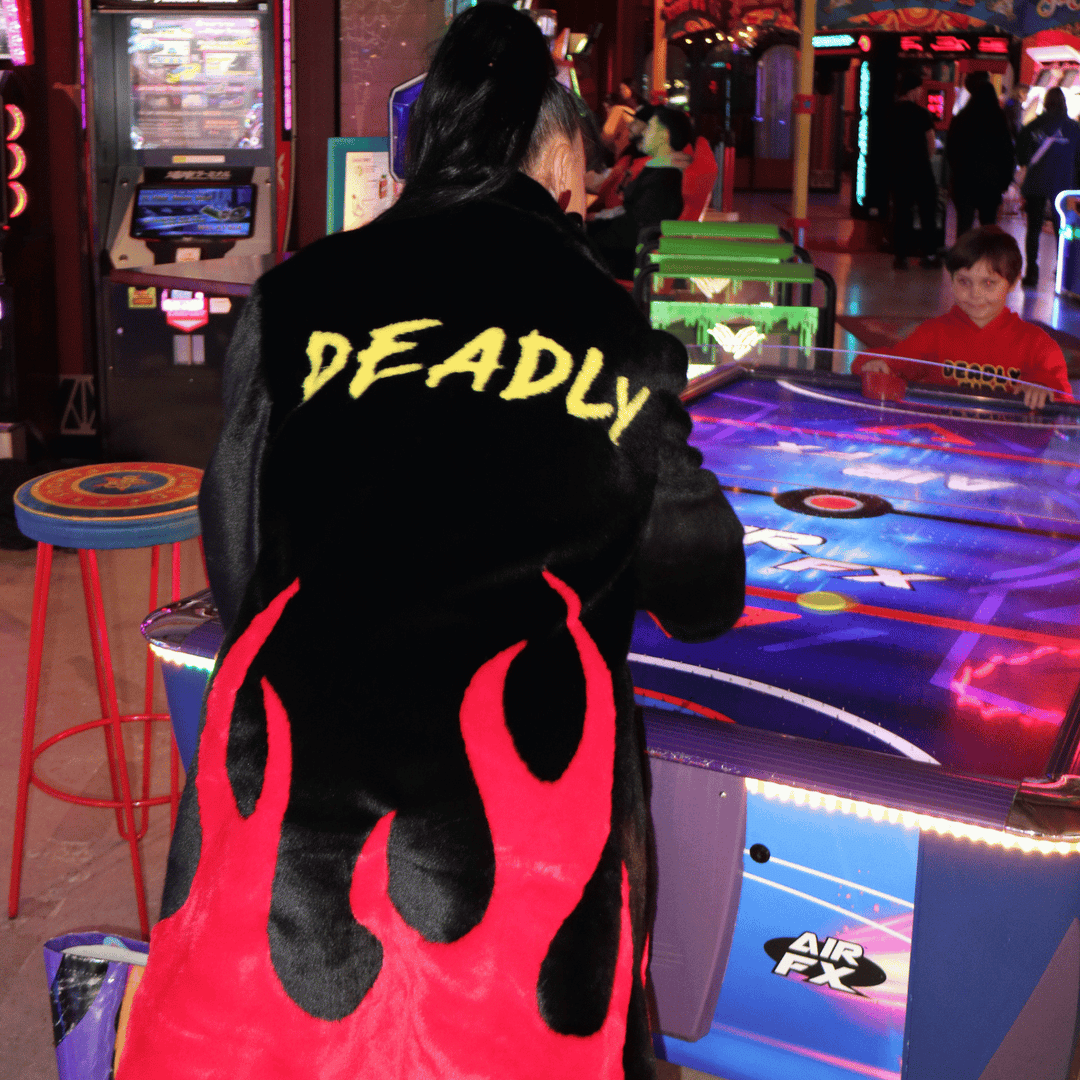 image of kristy from haus of dizzy wearing haus of dizzy x tibbs and bones deadly flamez fur jacket. it is a black knee length faux fur coat with red flames at the bottom and on the back it has 'deadly' in graffiti style yellow font