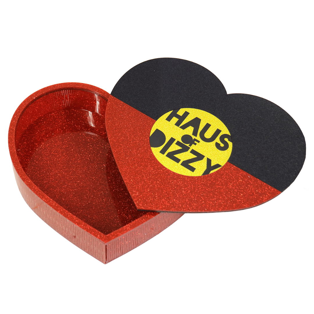 hand made heart-shaped acrylic jewellery box in Aboriginal flag colours. using black, yellow, and red glitter acrylic with hand painted haus of dizzy logo in yellow sun centre. box is half open with lid on top to show inside the box