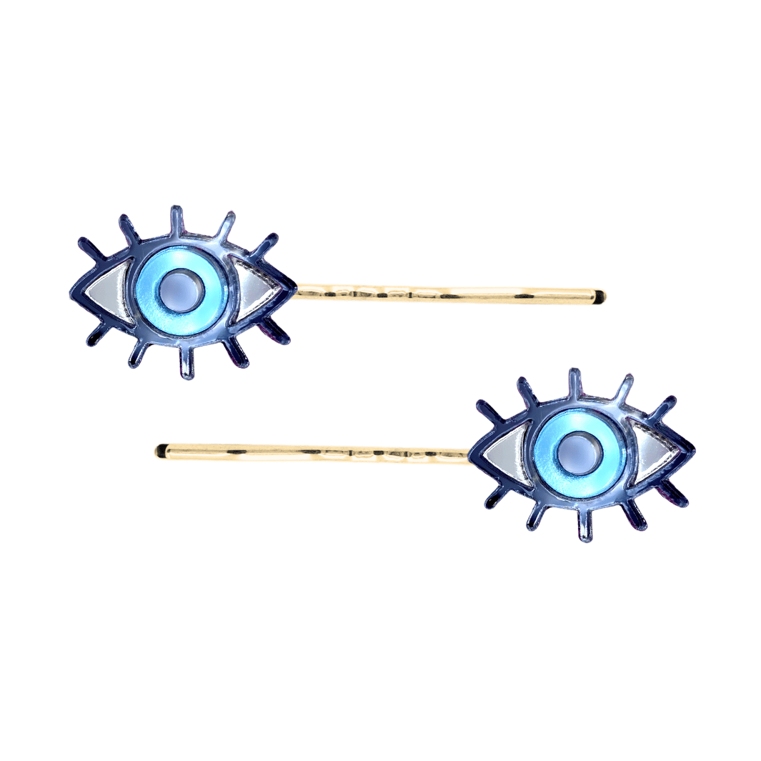 haus of dizzy eye see you hair pins set of two. Eye-shaped hair pins with blue mirror centers and gold hairpins on a white background