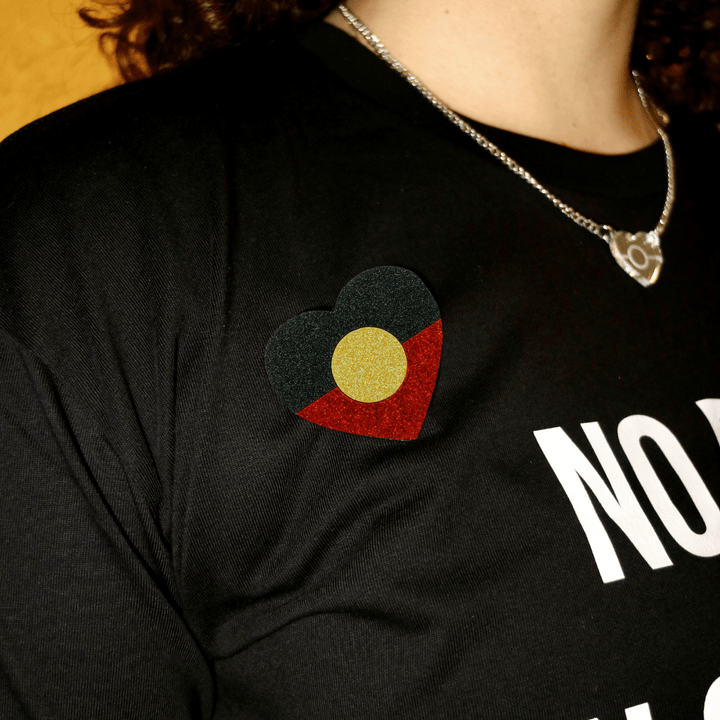 close up of model t-shirt wearing haus of dizzy's first nations pride glitter heart pin in the Aboriginal flag