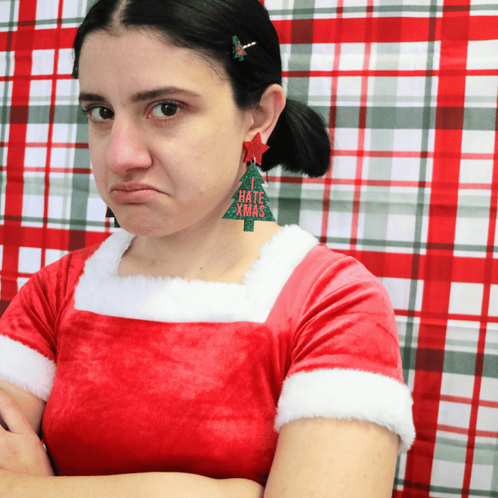 model wearing santa outfit with haus of dizzy i hate xmas earrings size large, looking at camera with unhappy face