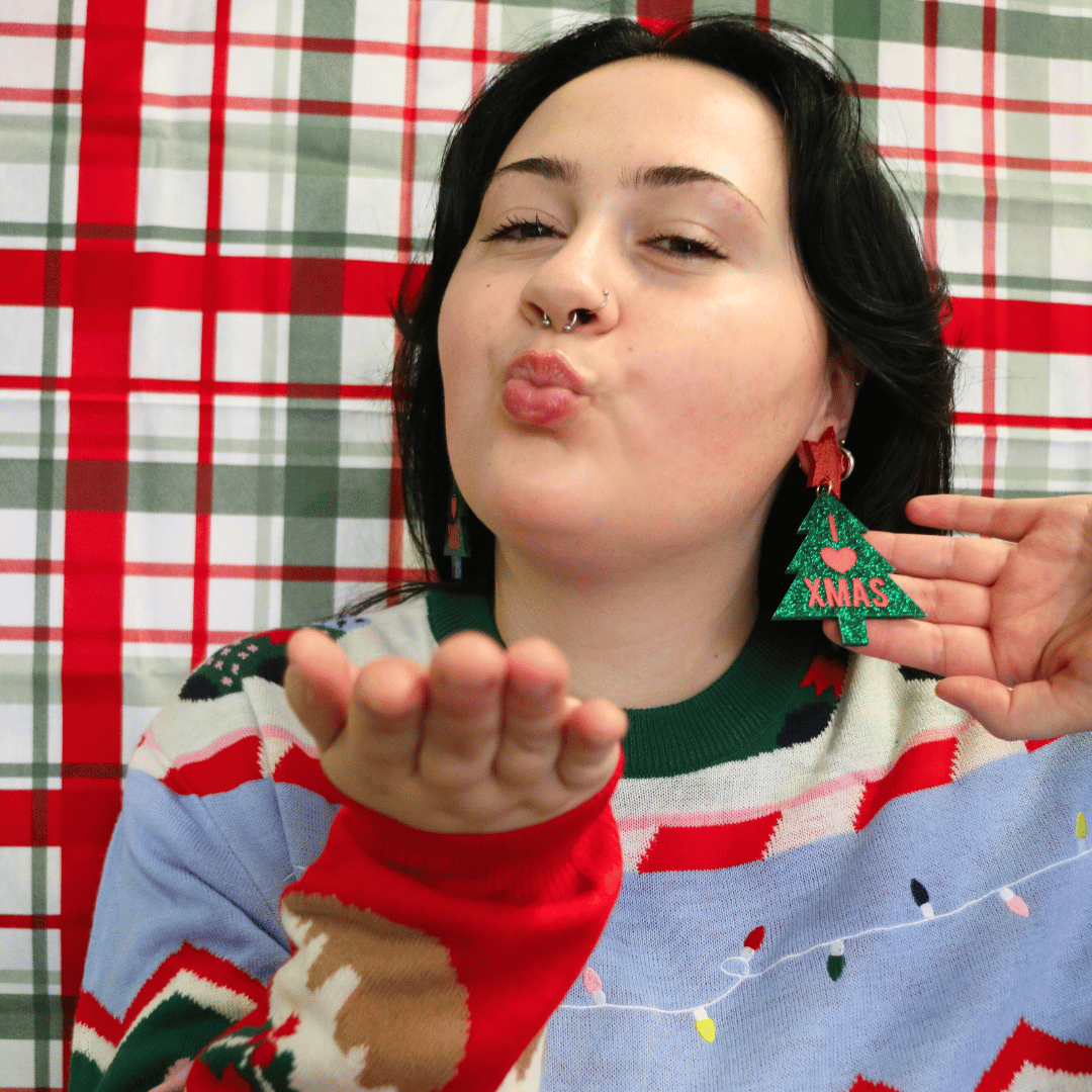 model wearing ugly christmas sweater with haus of dizzy i love xmas earrings size large, blowing a kiss at the camera